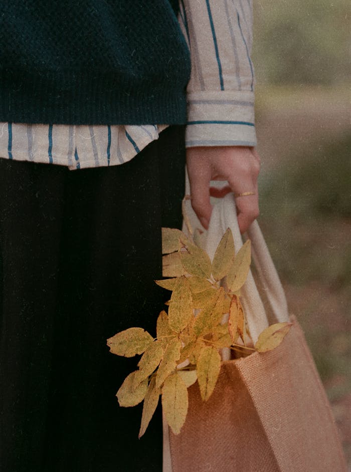 why-choose-us Close-up of a woman holding a bag with yellow autumn leaves, showcasing fall fashion.