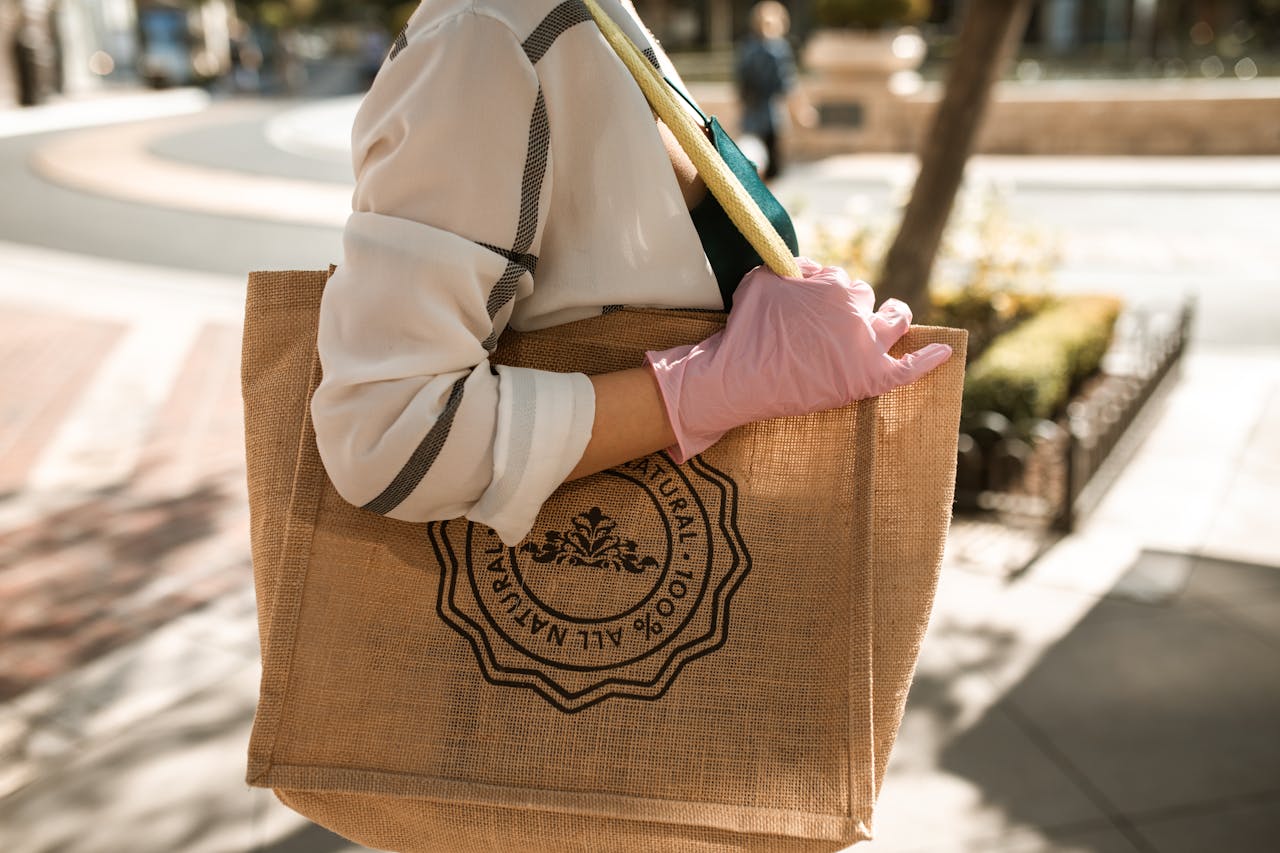 gallery-1 Close-up of a person with a brown tote bag and pink glove, outdoors on a sunny day.